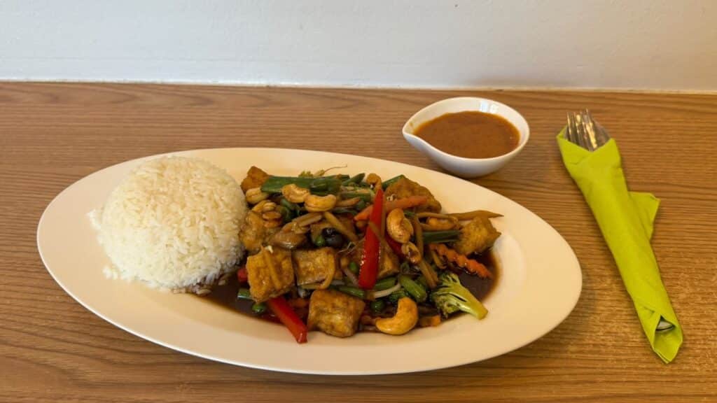 Phad Med Ma Muang vegan mit Tofu und Cashewkernen, daneben Reis und ein Schälchen Sauce